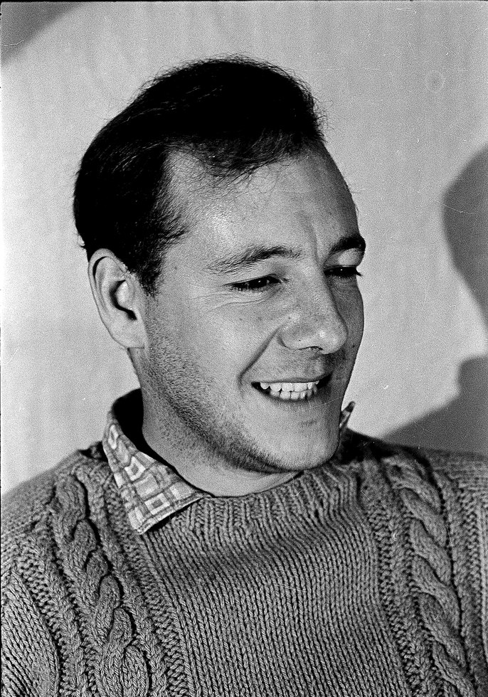 Head-and-shoulders portrait of Derek Distel at about thirty, smiling, in a cable-knit jumper